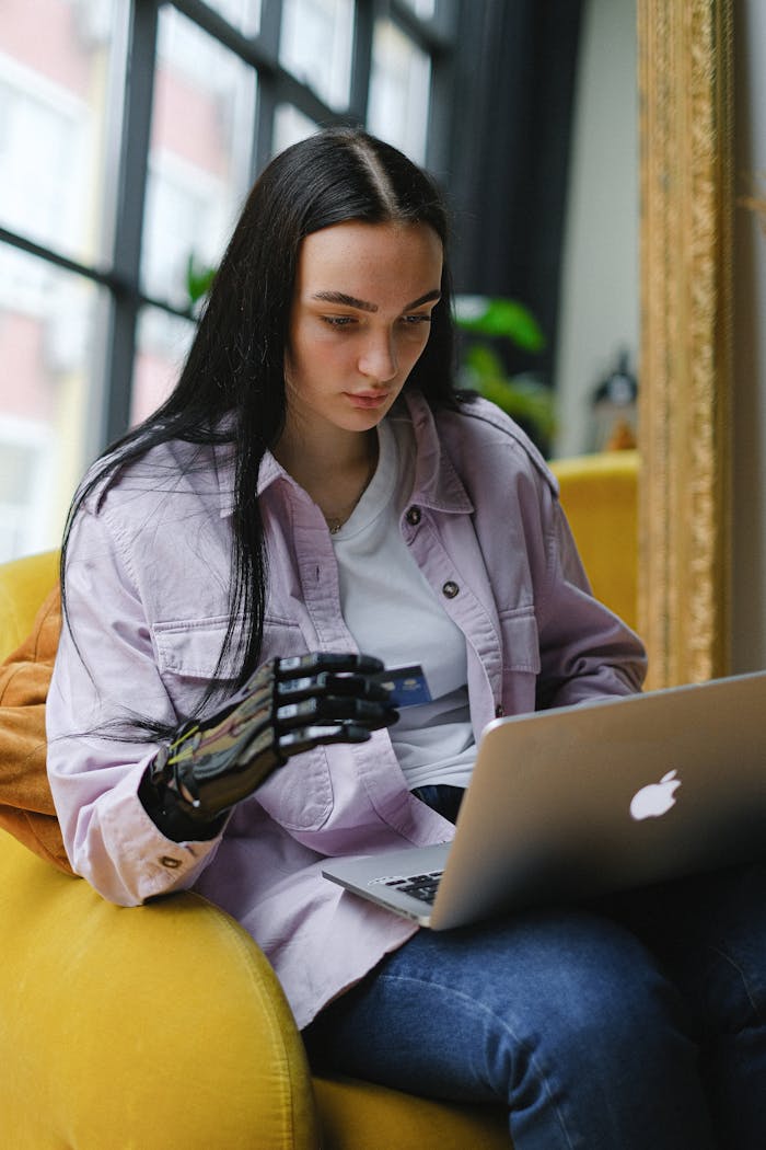 A woman with a prosthetic arm uses a laptop indoors for online shopping.